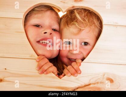 Primo piano ritratto carino sorelle peering attraverso la forma del cuore in legno Foto Stock