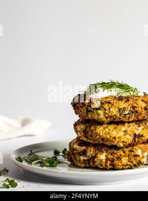 Cena - quinoa al forno vegano e frittelle di zucchine pronte per essere servite, con aneto fresco, micro erbe e panna acida vegana. Foto Stock