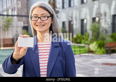Donna di affari matura che tiene una scheda di plastica vuota e sorridente Foto Stock