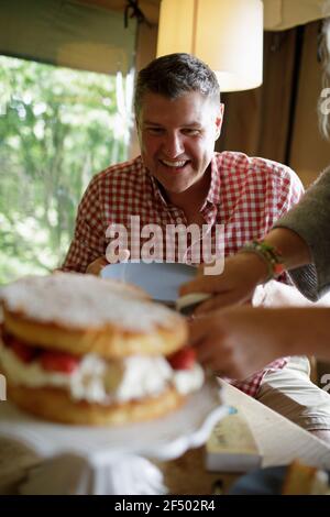Uomo felice guardando moglie fetta e servire torta di fragole Foto Stock