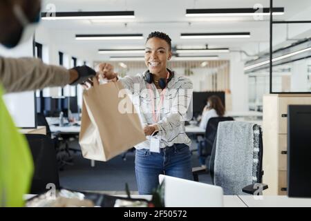 Donna d'affari felice che riceve la consegna del pranzo dal corriere in ufficio Foto Stock
