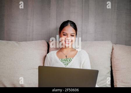 Bella giovane donna asiatica sorridente che lavora su un computer portatile in salotto a casa. Donna di affari dell'Asia che lavora nel suo ufficio domestico. Godendo del tempo a casa. Foto Stock