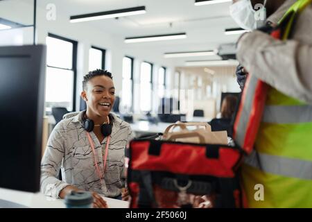 Donna d'affari che riceve la consegna del cibo dal corriere in maschera facciale Foto Stock