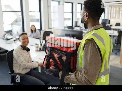 Donna d'affari che riceve la consegna del cibo dal corriere in maschera facciale Foto Stock
