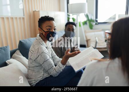 Uomini d'affari in maschere di faccia che discutono i documenti in riunione d'ufficio Foto Stock