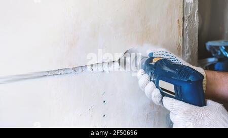 operaio fora un buco per una presa elettrica in una parete di mattoni di calcestruzzo. riparazione di elettrico wiring. operaio di costruzione con un martello pneumatico trapano Foto Stock