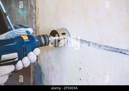 un lavoratore fora un foro per una presa elettrica in una parete di mattoni di calcestruzzo. riparazione di cablaggio elettrico. Uomo addetto alla costruzione con martello pneumatico d Foto Stock