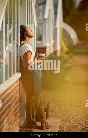 Serena donna giardino negozio proprietario crogiolarsi alla luce del sole con caffè Foto Stock