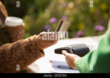 Primo piano donna che paga cameriera con carta di credito su soleggiato patio Foto Stock