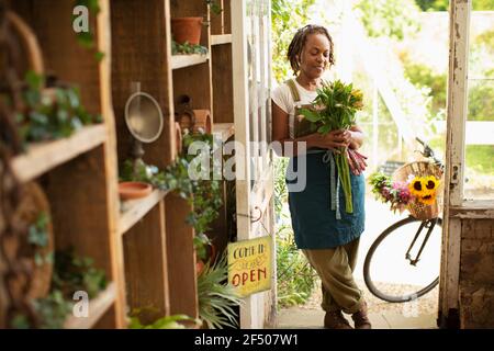 Fiorista femminile che tiene bouquet di fiori nella porta del negozio Foto Stock