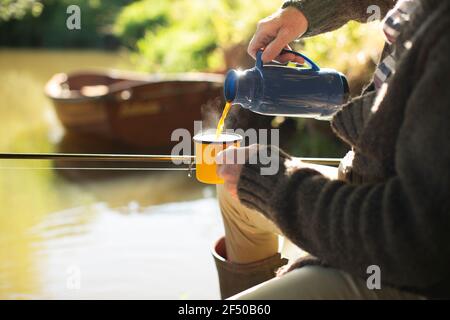 L'uomo pesca a mosca e versa il caffè al fiume soleggiato