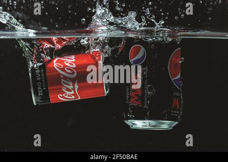 Vista ravvicinata di due lattine che cadono in acqua. Coca cola vs Pepsi cola. Foto Stock