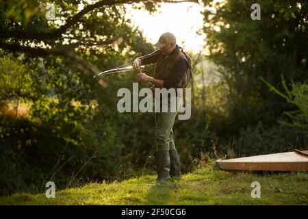 Uomo che prepara la lenza di pesca del mosca alla riva del fiume Foto Stock