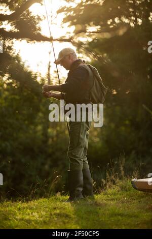 Uomo che prepara pesca a mosca palo in riva al fiume Foto Stock
