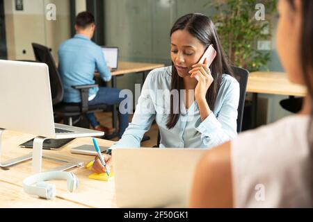 Imprenditrice parlando al cellulare alla scrivania in ufficio Foto Stock
