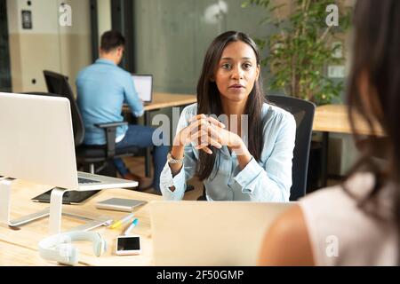 Donna d'affari attenta che ascolta la collega in ufficio Foto Stock