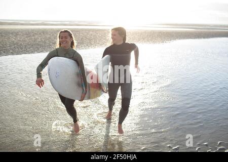 Felici giovani surfisti che corrono con tavole da surf nell'oceano soleggiato surf Foto Stock