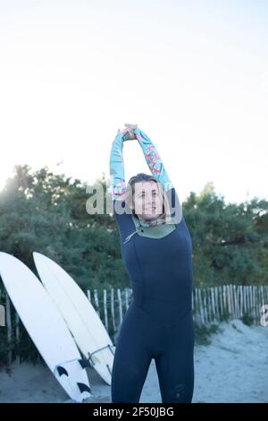 Giovane surfista femminile in tuta bagnata che allunga le braccia sulla spiaggia Foto Stock