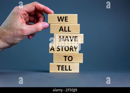 Abbiamo tutti una storia da raccontare Symbol. Blocchi di legno con parole 'abbiamo tutti una storia da raccontare'. Mano uomo d'affari. Splendido sfondo grigio. Business, pop Foto Stock