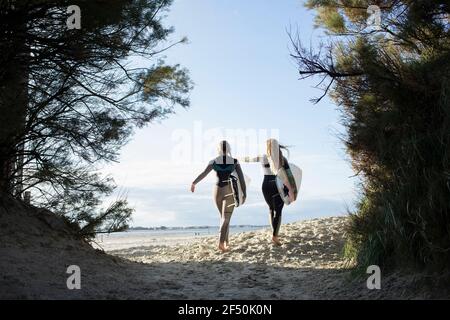 Giovani surfisti donne che corrono con tavole da surf su un soleggiato sentiero da spiaggia Foto Stock