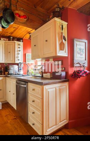 Mobili in legno di quercia verniciato bianco e ripiani in ceramica tonalità terra sfumata in cucina con pavimenti in legno di pino, pareti dipinte di rosso all'interno della vecchia casa Foto Stock