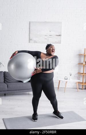 donna afroamericana più grande stupita in sportswear che tiene il fitness sfera Foto Stock