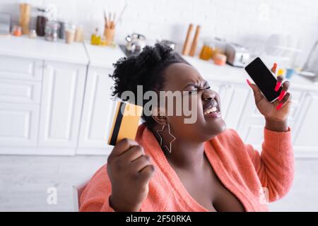 ha stressato african american più la donna di taglia che tiene la carta di credito e. smartphone Foto Stock
