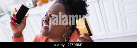 stressato afroamericano più la donna di taglia che tiene la carta di credito e lo smartphone, la bandiera Foto Stock