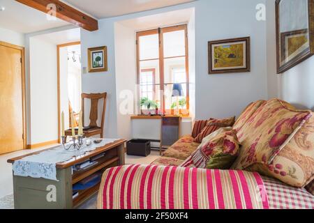 Divano letto a scacchi rosso, beige, grigio con seduta e cuscini in fiore, tavolino da caffè in legno e seggiolone con sedile in pelle nera rivettata Foto Stock