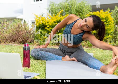 Donna caucasica che pratica yoga e utilizza il computer portatile in giardino Foto Stock