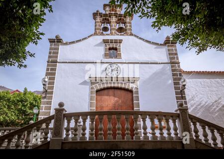 Vista ad angolo basso della facciata di una piccola chiesa dipinta in bianco con un orologio sopra la porta Foto Stock