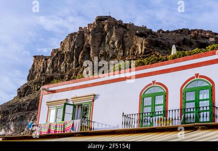 Particolare della facciata di una casa dipinta in bianco e rosso, con diverse finestre e balconi e una montagna rocciosa sullo sfondo Foto Stock