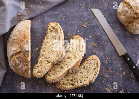 immagine zenitale di un pane ecologico con taglio a coltello in fette poste a ventaglio su un buio superficie circondata da briciole e un panno grigio con n. Foto Stock