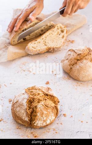 immagine verticale di tre pani organici disposti a forma di triangolo, uno dei quali spezzato in fette su una superficie bianca e un bordo di tessuto beige Foto Stock