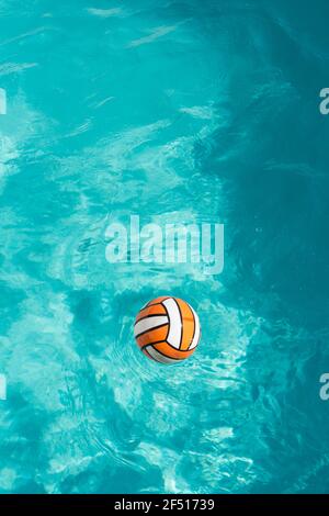 immagine verticale di una sfera arancione e bianca che galleggia a. il fondo del colpo in una piscina blu turchese Foto Stock