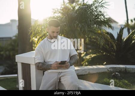 Scatto a basso angolo di un uomo europeo seduto all'aperto e. sms sul suo telefono Foto Stock