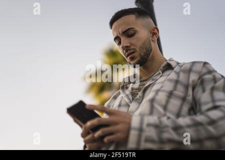 Tiro a basso angolo di un uomo europeo in una plaid maglietta sul suo telefono Foto Stock