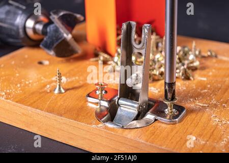 Montaggio di cerniere metalliche sul truciolare. Lavoro di Falegnameria durante l'assemblaggio dei mobili domestici. Sfondo scuro. Foto Stock