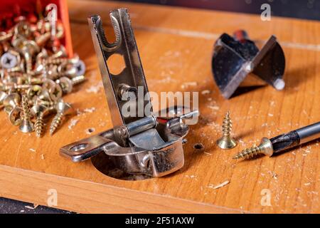 Montaggio di cerniere metalliche sul truciolare. Lavoro di Falegnameria durante l'assemblaggio dei mobili domestici. Sfondo scuro. Foto Stock