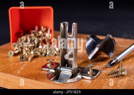 Montaggio di cerniere metalliche sul truciolare. Lavoro di Falegnameria durante l'assemblaggio dei mobili domestici. Sfondo scuro. Foto Stock