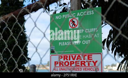 Segnale di avvertimento verde visto attraverso una recinzione a catena; scogliera ripida, habitat sensibile, proprietà privata; Isola di Yerba Buena, San Francisco, Caifornia. Foto Stock