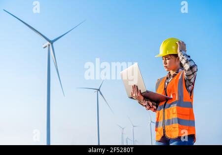 giovane ha sottolineato femmina ingegnere che ha problemi a lavorare con il portatile computer contro l'azienda agricola di turbine eoliche Foto Stock