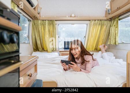 Giovane donna che usa uno smartphone sul letto di un camper van motorhome Foto Stock