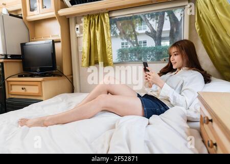 Giovane donna che usa uno smartphone sul letto di un camper van motorhome Foto Stock