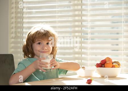 Cibo e bevande per i bambini. Divertente felice capretto carino con il latte di bevanda di vetro siedono in cucina. I bambini sani godono di yogurt, concetto di nutrizione sanitaria per i bambini Foto Stock