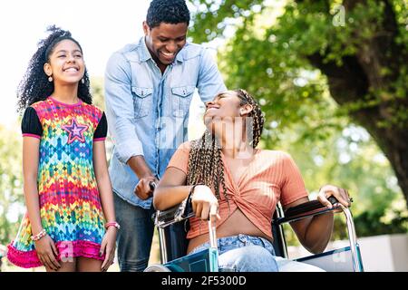 Donna in sedia a rotelle che si gode una passeggiata con la famiglia. Foto Stock