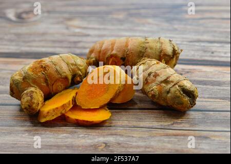 Primo piano di fette e radice curcica intera o rizoma. Native del subcontinente indiano, le radici sono usate in cucina & medicina ayurvedica. Foto Stock