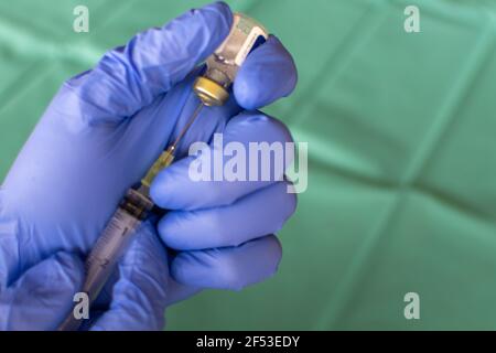 Mano dell'operatore sanitario in guanto viola preparazione di una siringa davanti a un panno chirurgico. Primo piano di una mano chirurgo con un vaccino. Una siringa con Th Foto Stock