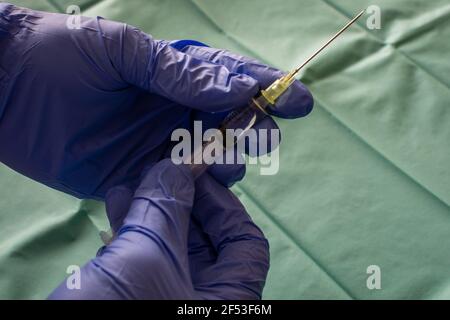 La mano dell'operatore sanitario nel guanto viola tiene la siringa contro un panno chirurgico. Primo piano di una mano chirurgo con un vaccino. Una siringa con il vaccino. Foto Stock