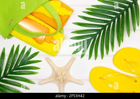 Estate mare spiaggia vacanza composizione creativa. Borsa con asciugamani e crema solare, sandali infradito, stelle marine, foglie di palma tropicali Foto Stock